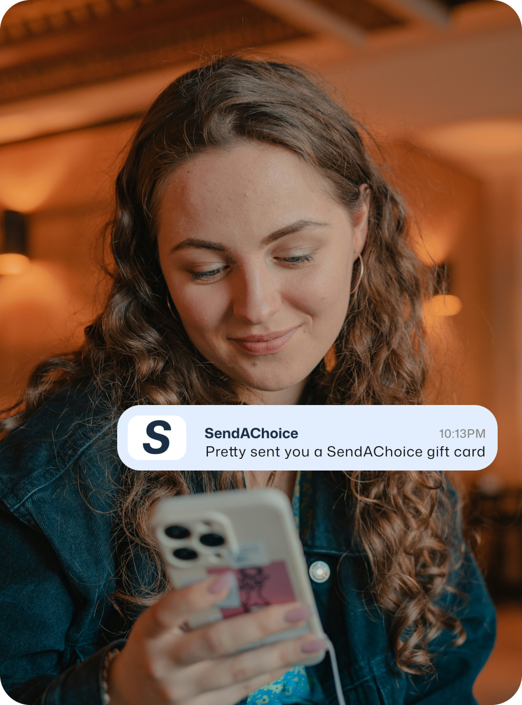 A picture of a woman smiling at a phone and receiving a scheduled SendaChoicegift card